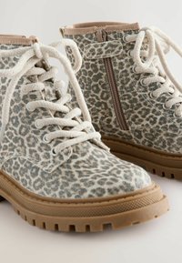 Botas de tobillo con estampado de leopardo, hechas de un tejido texturizado, con un diseño de cordones beige y cremallera lateral. Suela de goma gruesa que proporciona tracción.
