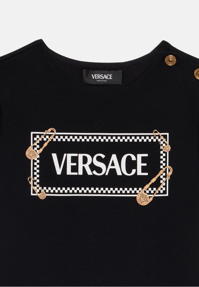 Svart bomull T-skjorte med hvit trykket "VERSACE"-logo, gull sikkerhetsnåler og et rutete borderdesign. Rund hals med knappdetaljer.