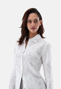 Camicia bianca a maniche lunghe con un delicato motivo a farfalle, chiusura anteriore con bottoni e colletto classico, realizzata in leggero tessuto di lino.
