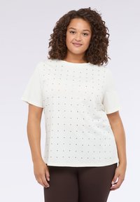 Camiseta blanca de manga corta y escote redondo, que presenta un patrón de cuadrícula de pequeños clavos plateados en la parte delantera.