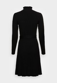 Czarna sukienka z prążkowanego materiału, z długimi rękawami, dopasowaną górą i rozkloszowanym dołem. Posiada wysoki dekolt z falbanką oraz pasujący pasek w talii.