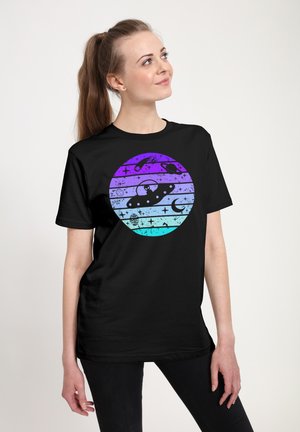 Kvinde står og kigger op, iført en sort trøje med en lilla og blå cirkel med grafik af et UFO, stjerner, planeter og en halvmåne.