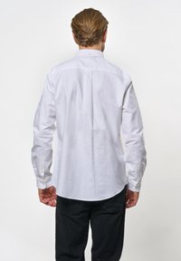 Vit långärmad skjorta med rundad nederkant, mittveck bak och knappmanschetter. Tillverkad av ett mjukt, lätt tyg.