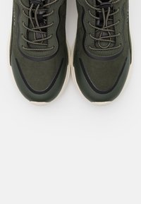 Baskets en daim vert avec accents noirs élégants, design à bout rond et lacets texturés, dotées d'une semelle épaisse en caoutchouc crème.