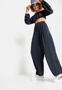 Top corto de un oscuro azul marino con mangas abullonadas, combinado con pantalones de pierna ancha y fluidos. Zapatillas de plataforma blancas con acentos coloridos completan el look.