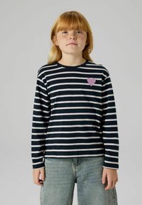 Schwarz-weiß gestreiftes Langarmshirt mit pinkfarbenem Glitzerherz auf der linken Brust, kombiniert mit hellblauen Jeans.