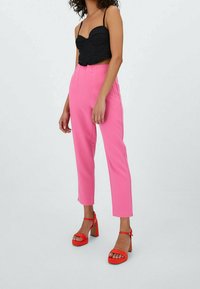 Haut court noir ajusté avec fines bretelles, associé à un pantalon rose taille haute à jambes droites et des sandales rouges à talons blocs.