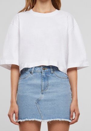Kobieta w białym krótkim t-shircie i jasnoniebieskiej jeansowej mini spódnicy z postrzępionym dołem.