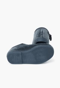 Mule de ante gris con una textura suave, suela de goma y un distintivo acento de hebilla. Presenta una forma redonda y un diseño de perfil bajo.