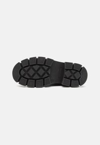 Semelle de chaussure en caoutchouc noir avec un motif de crampons en zigzag et des formes rectangulaires et imbriquées surélevées pour une meilleure adhérence. Design de talon plat.