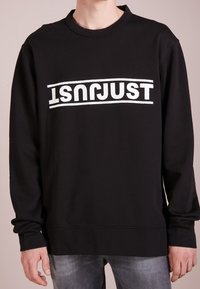 Sudadera negra con un gran gráfico en blanco que dice "JUST", cuello redondo, mangas largas y un corte relajado. Material suave con puños acanalados.