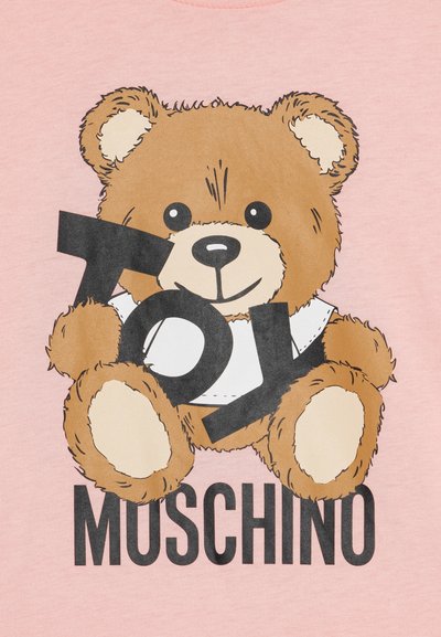 Camicia rosa chiaro con un orsetto dei cartoni animati che tiene un ritaglio nero a forma di "TOY", con la parola "MUSCHINO" stampata in grassetto sottostante.