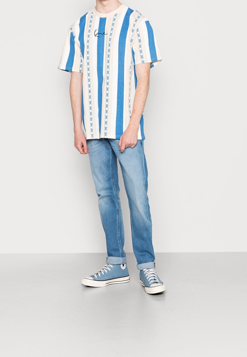 Randig T-shirt i blått och krämfärgat bomull, med en logotyp. Matchas med ljusblå jeans och blå kanvas sneakers med vita detaljer.