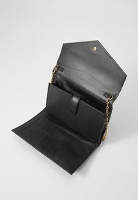 Portafoglio in pelle vegana nera con pattina esagonale, tracolla in catena dorata, vari slot per carte e compartimento con zip.