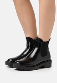 Bottes chelsea en cuir noir avec des panneaux élastiques latéraux, doublure intérieure texturée et semelles robustes pour une bonne adhérence. Fini lisse et bout rond.