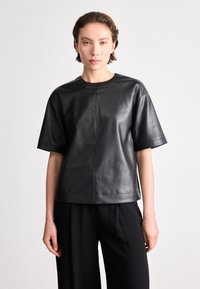 Top curto de manga curta em couro preto com decote redondo e corte reto. Textura lisa com costuras visíveis e detalhes de design minimalistas.