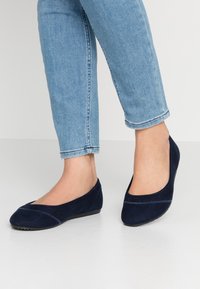 Ballerines en suede bleu marine avec un bout arrondi et des coutures, associées à un jean en denim léger aux chevilles.