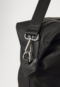 Black nylon handbag featuring a zipper closure, metal hardware, and a textured strap with a leather accent for added durability.