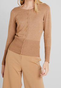 Hellbraune Strickjacke aus gestricktem Stoff, mit geripptem Saum und Bündchen, Knopfverschluss vorne und langen Ärmeln.