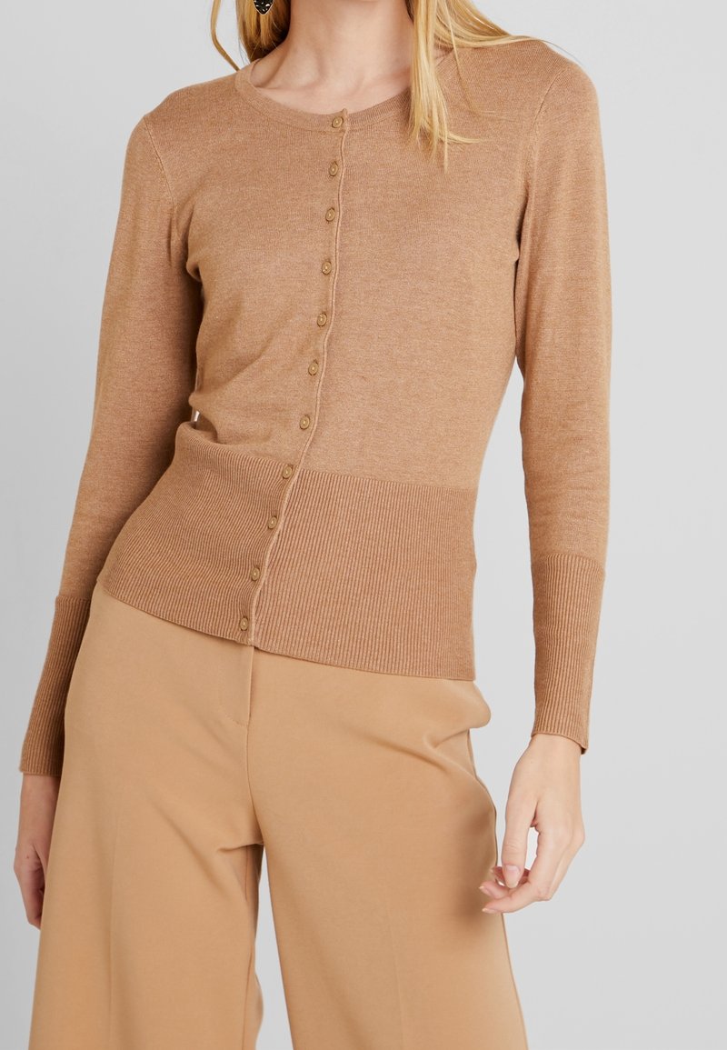 Hellbraune Strickjacke aus gestricktem Stoff, mit geripptem Saum und Bündchen, Knopfverschluss vorne und langen Ärmeln.