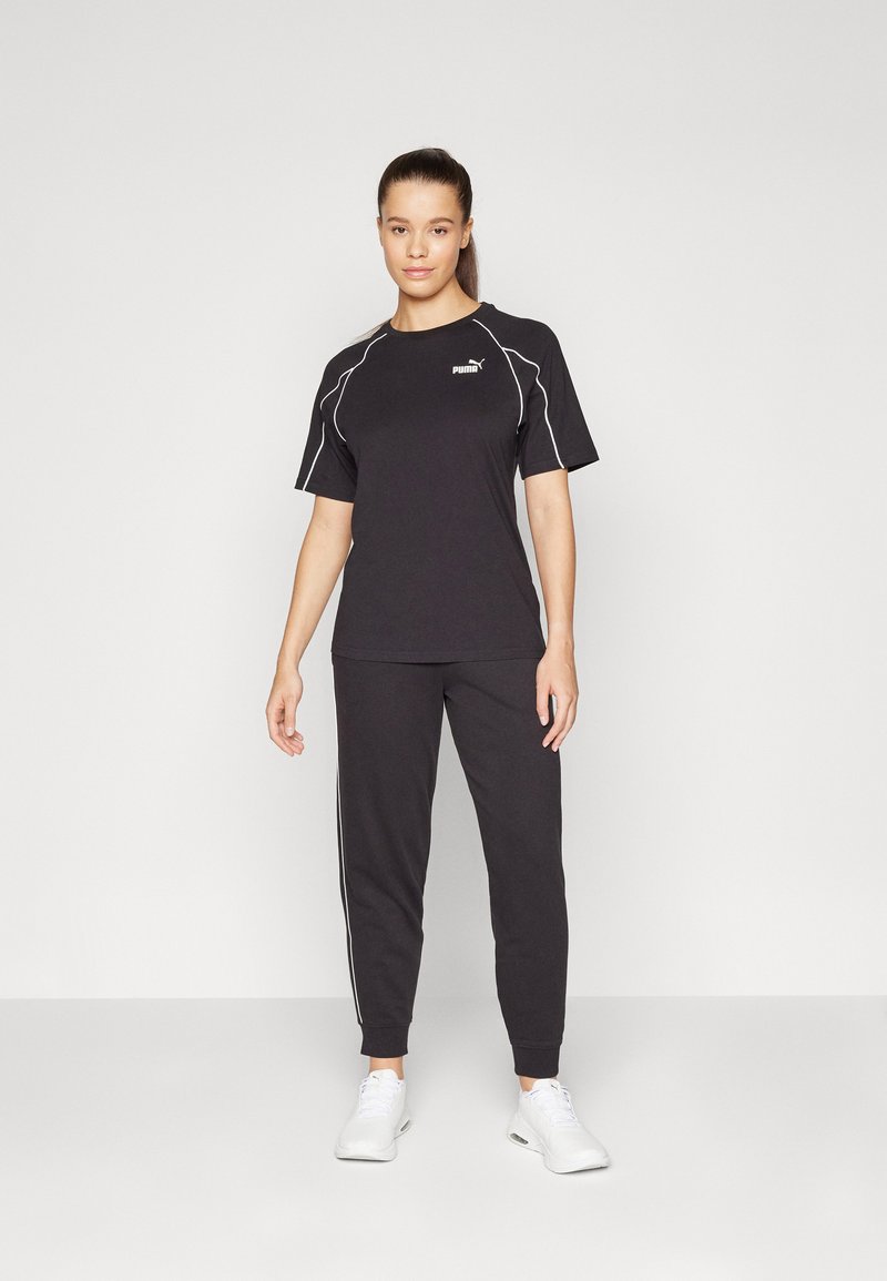 Completo sportivo nero composto da una maglietta a maniche corte con dettagli bianchi e pantaloni aderenti coordinati. Il modello indossa delle scarpe da ginnastica bianche.
