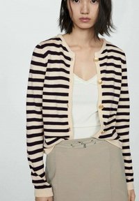 Cardigan a righe in crema e viola scuro, con bottoni rotondi dorati, polsini a coste e una vestibilità rilassata, indossato sopra una maglietta bianca.
