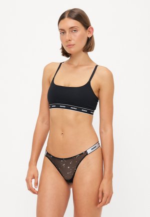 Black crop top with thin straps and branded elastic band; matching black sheer bikini with star pattern and contrasting logo waistband.