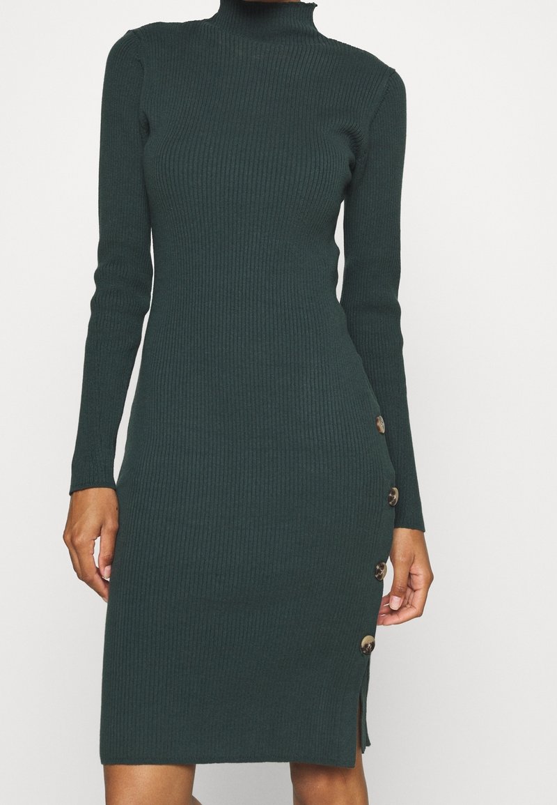 Ribbed turtleneck mekko tummassa vihreässä, jossa on pitkät hihat, istuva siluetti, sivupainikkeet ja polvipituinen leikkaus, jossa on sivu halkio.