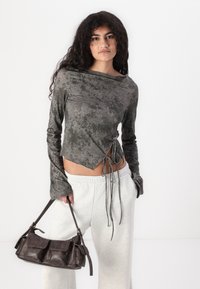 Donkergrijze langemouwen crop top met ronde halslijn en een trekkoord aan de zijkant, gecombineerd met lichtgrijze joggingbroek en een stijlvolle donkere handtas.