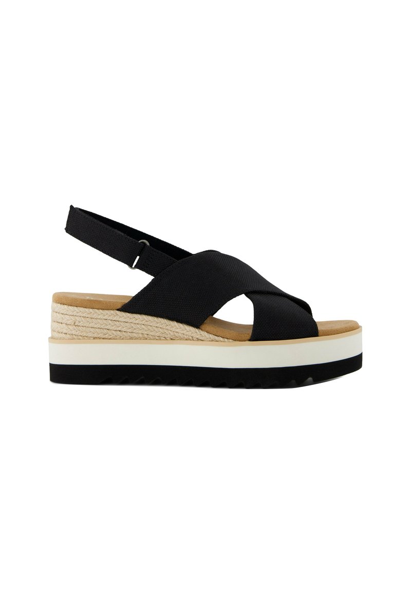 Svart textil sandal med korsade remmar, beige plattform, vit mellansula och svart strukturerad sula. Justerbar slingback för passform.