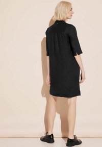 Schwarzes Leinenkleid mit einfachem Design, knielang, halbärmlig und lockerer Passform, mit einem dezenten Einschnitt auf der Rückseite.