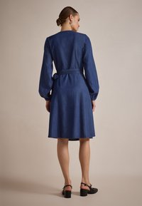 Denimkjole med lange ermer, rund hals og innsnevret midje. Har en glatt tekstur og en>A-skjørt, i en mørkeblå farge.