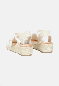 Sandali con zeppa in alto tessuto intrecciato argentato, cinturini in tessuto crema e suola avvolta in juta, con una cinghia posteriore per supporto e una soletta di colore beige neutro.