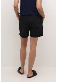 Pantalones cortos de mezclilla negra con dobladillos enrollados, que cuentan con dos bolsillos traseros, acentos mínimos de hardware y una textura suave. Se llevan con sandalias planas.