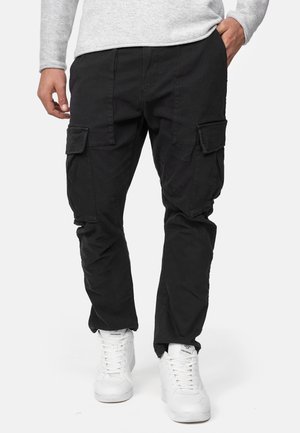 Pantaloni cargo neri con una vestibilità rilassata, dotati di molteplici tasche laterali, realizzati in tessuto resistente, abbinati a sneakers bianche.