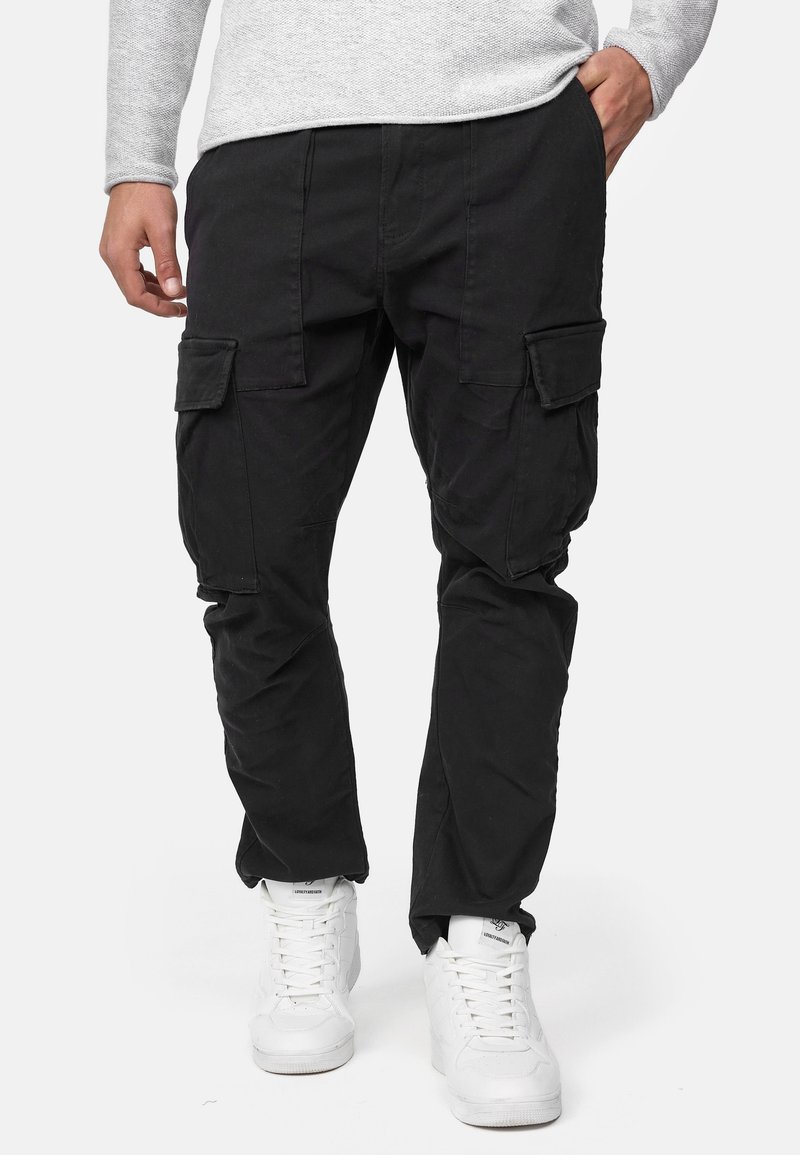 Schwarze Cargo-Hosen mit einem lockeren Schnitt, ausgestattet mit mehreren Seitentaschen, aus strapazierfähigem Stoff, kombiniert mit weißen Sneakern.