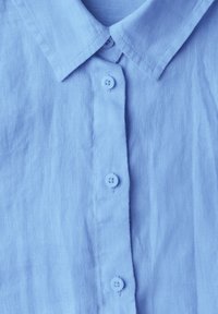 Camicia azzurra chiara con un tessuto morbido e testurizzato; presenta un colletto a punta e cinque bottoni coordinati lungo la patta frontale.