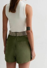 Olivengrüne Shorts mit Gesäßtaschen, strukturiertem Bund mit einem weißen geometrischen Muster, kombiniert mit einem figurbetonten weißen ärmellosen Oberteil.