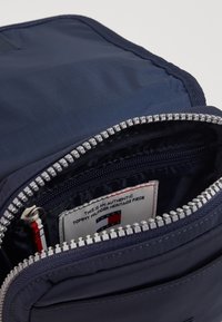 Borsa in nylon blu navy con una superficie liscia, dotata di una zip argento e un'etichetta con accenti rosso, bianco e blu all'interno della tasca principale.