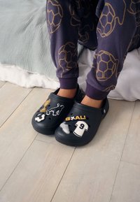 Saboti bleumarin cu autocolante decorative, inclusiv un trofeu, o minge de fotbal, textul „GOAL!” și un tricou de fotbal, având găuri de ventilație și talpă texturată.