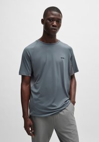 T-shirt de sport gris à manches courtes avec un col rond, arborant un logo de marque discret sur le côté gauche et une texture légère et lisse.