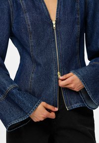 Jeans jakna z globokim V-izrezom, dolgimi zvonastimi rokavi, z zlatim zadrgo in kontrastnimi šivi v temno modri tkanini.