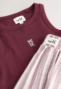 Bordeauxrotes, geripptes Tanktop und rosa-weiß gestreifte Unterteile mit "self." Markenetiketten und besticktem Logo im Brustbereich.
