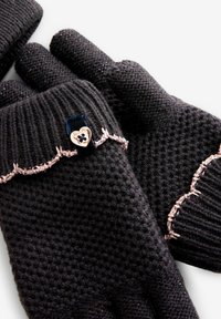 Mustat neulotut käsineet, joissa on kuvioitu pinta, vaaleanpunaisella ommeltu reunus ja pieni sydämenmuotoinen nappi toisen käsineen rannekkeessa.