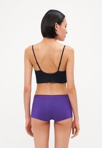Svart bralette med tynne stropper, paret med lilla boyshorts med et kontrasterende liv, glatt stoff og en tettsittende design.