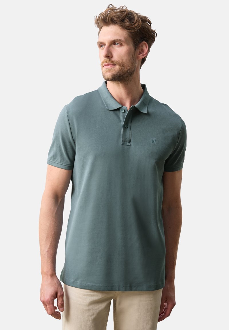 Pikétröja i dämpad teal-färg, kortärm, treknappsknäppning, mjukt bomullsmaterial och subtil logotypdetalj på bröstet.