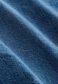 Blauwe denimstof met zichtbare dichte weefstructuur en diagonale plooien die licht- en schaduwcontrast creëren.