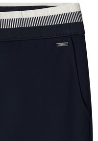 Marineblauwe broek met witte en marineblauwe geribde tailleband, zijzak en klein metalen merkteken vlak bij de zak.