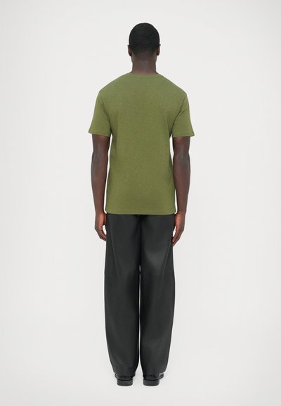 Λαδί πράσινο μπλουζάκι με κοντά μανίκια και στρογγυλή λαιμόκοψη, συνδυασμένο με φαρδιά μαύρη παντελόνια· λεία υφή, μινιμαλιστικός σχεδιασμός.