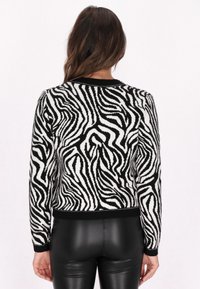 Pulover z zebrastrukturo v črno-beli barvi z rebrastimi manšetami in ovratnikom; izdelan iz mehkega pletenega materiala; enobarvna črna obroba in detajli.